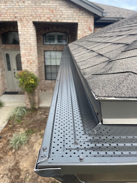 Dark bronze Bulldog Gutter Guard installed at a roof corner beside asphalt shingles